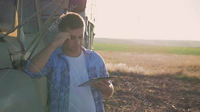 A pensive farmer is working in the field. Uses a tablet, stands near the agricultural engineering.
