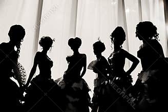 Black and white image of the silhouette of girls and women in carnival costumes and ball dresses in the theater on the stage behin