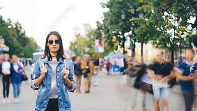 Time-lapse of lonely girl tourist standing in modern city with people moving around and looking at camera. Youth