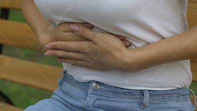 Woman feels strong pain in upper abdomen and sits on bench, gastritis, heartburn