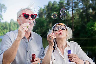 Cute aged couple wearing funny glasses and blowing soap bubbles
