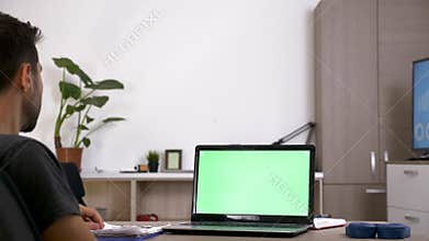 Man at his desk in front of computer with green screen