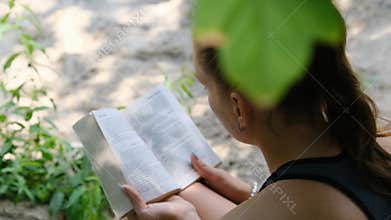 Young Woman Reads a Book Sitting on the Grass in Nature at Summer Day
