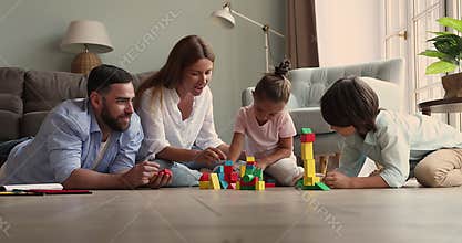 Mom dad and kids construct buildings from blocks on floor