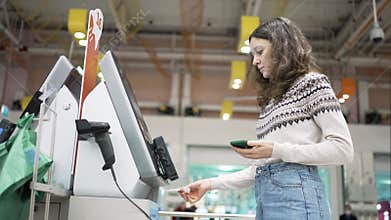 Brunette woman pays at self-checkout point and gets receipt