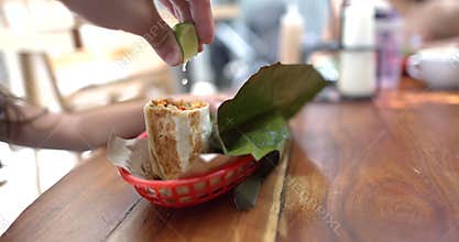 Hand squeezing lime onto tasty burritos on wooden table