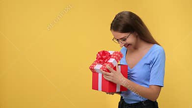 Overjoyed young blonde woman opening festive red package bow celebrating seasonal holiday isolated