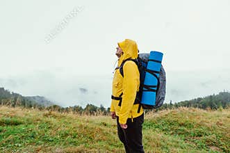 Man in a yellow raincoat in a mountain hike in rainy weather on a background of landscapes with clouds
