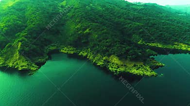 erial view flying over a tropical land with a village on it and a forest in the background surrounded by river,