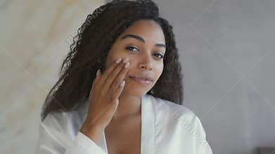 Mirror pov of young attractive african american lady applying moisturizing cream on face, taking care about appearance