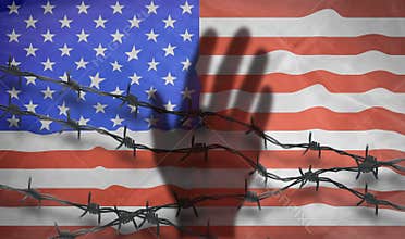 The shadow of the hand behind the barbed wire on the background of the American flag.Metal fence with barbed wire on a USA flag.