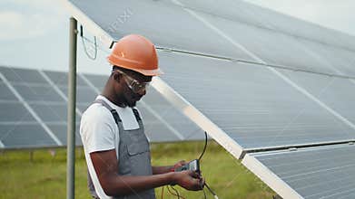 African american man in grey overalls measuring resistance in solar panels outdoors. African man in overalls measuring