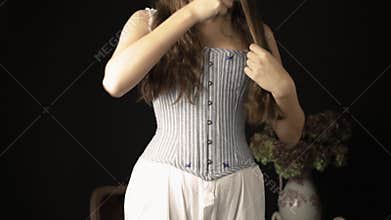 A Victorian woman wearing a corset and combinations and brushing her hair with a silver-backed hairbrush