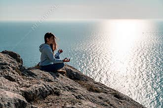 Woman tourist enjoying the sunset over the sea mountain landscape. Sits outdoors on a rock above the sea. She is wearing