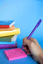Vertical photograph of stacked books with the colors of the lgtb flag and a hand writing love on a postit. copy space and blue
