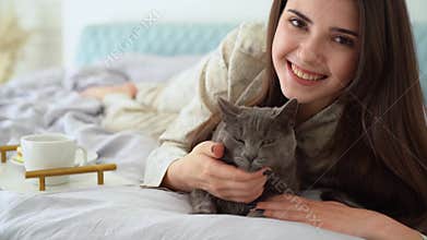 Young woman having breakfast in bed, stroking and kissing cat