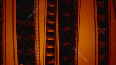 Camera movement over old film negatives in red light. Retro tape filmstrip with picture, close up. Analog old strips of