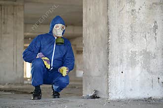 Worker in gas mask and protection suit at project site near dead bird