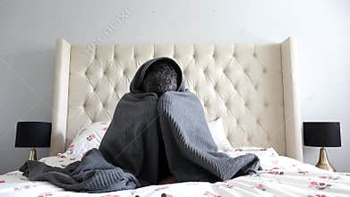 Afraid adult man covered in blanket sitting on bed