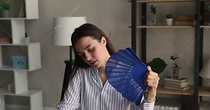 Unhappy young business woman blowing cool air with paper fan.