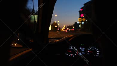 Driving around city at night by car, speed drops from 50 to 30 kilometers per hour. Rear view of driver out of focus and