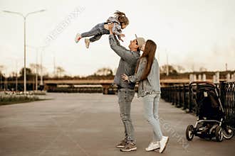 Stylish young family dressed in denim clothes walks near the river with a stroller