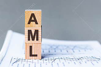 Three wooden cubes with letters - AML - ANTI-MONEY LAUNDERING, on grey table, space for text in left. Front view concepts