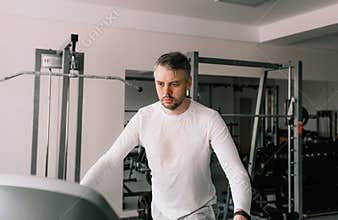 a tired man in a sweat-soaked T-shirt runs on a treadmill in a sports club. cardio workout