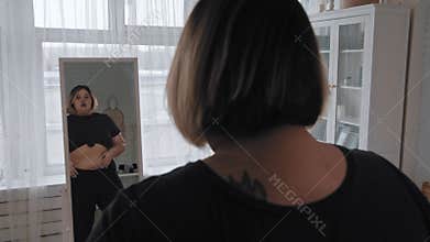 A fat woman looking at herself in the mirror and examines her body in crop top