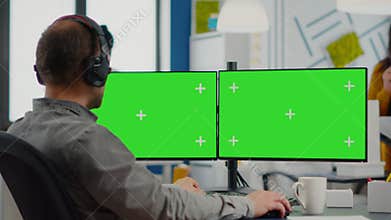 Employee with headphones working in dual monitror setup with green screen