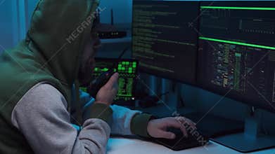 Anonymous computer hacker using laptop computer for cyber attack and calling on cellphone. Darknet and cyber security