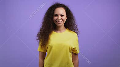 Young woman with curly hair looking to camera, smiling. Beautiful mixed race model lady on violet studio background