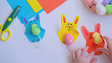 Childrens hands put an Easter egg of a paper bunny craft.