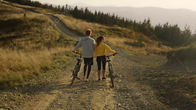 Woman and man with bikes walking on road. Couple taking break after cycling