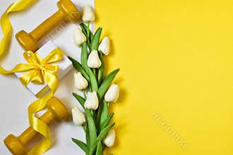 Yellow dumbbells, gift present with boquet tulips on a yellow and white background.Healthy fitness. Postcard for Valentine`s Day,