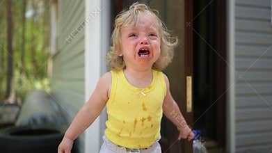 Close up portrait of little funny cute blonde girl child toddler in yellow dirty bodysuit crying outside at summer