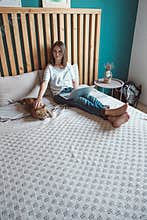 Young woman using laptop to work, lying on the bed with a pet cat in the bedroom, . Flexible hours and remote work.