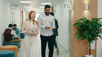 A handsome black man is walking with a stunning ginger woman, they are work colleagues and the black man is holding a