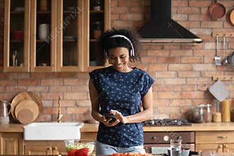 Excited Black teen student girl in headphones cooking to music