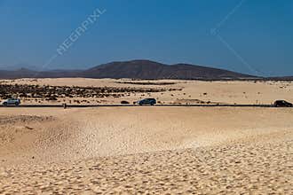 Road a cross desert with cars parked on the side.