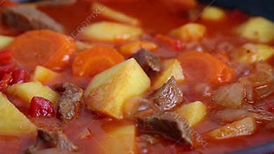 Beef stew with potatoes and carrots in red pot, boils and gurgles, close-up.