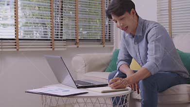 Asian man on laptop, writing, taking notes, watching webinars, training, participating in internet class, motivated positive