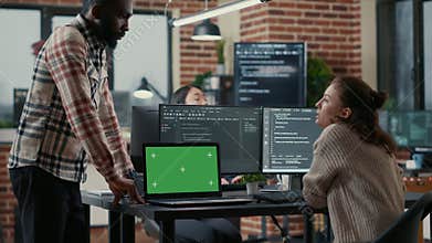Programer working at desk with multiple computer screens and laptop with green screen chroma key mockup
