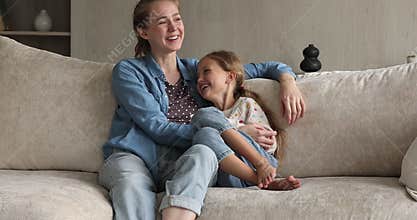 Loving foster mother and preteen adopted daughter cuddle on sofa