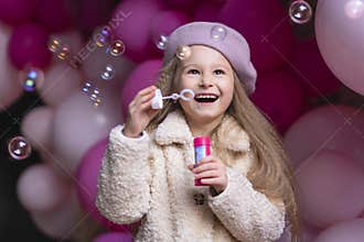 Happy smiling, laughing little girl in beret playing with pink, purple balloons, soap bubbles