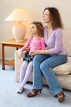 Mother and daughter sits on couch in cozy room