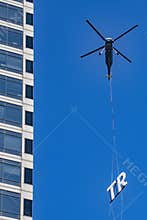 Commercial Helicopter carries a sign part to the top of a skyscraper