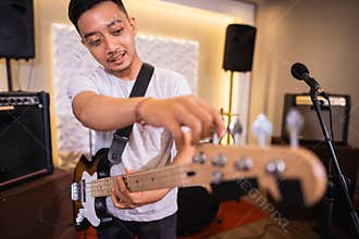 a male bassist tunes an electric guitar bass string before playing