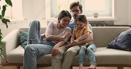 Young family couple with little daughter cuddle on couch