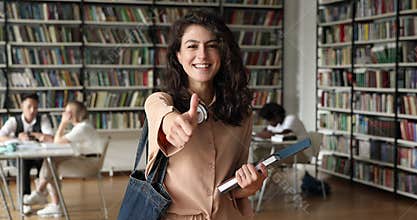 Happy student girl standing in campus library showing thumbs up